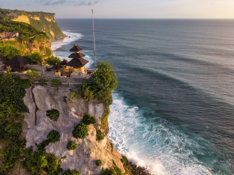 Aerial view of Uluwatu Temple perched on a cliff in Bali, Indonesia, at sunset.